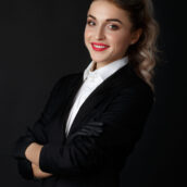 Sexy smart blonde with long curly hair poses in black jacket and black gloves in a dark studio